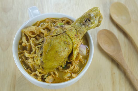 noodle dish in a yellow curry with chicken in white bowl on wooden background with spoon