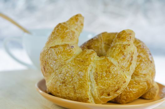 close up  croissants on  brown dish  and a white  cup of coffee with spoon