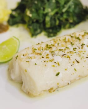 close up fillet fish steak with spinach  and lime on white plate