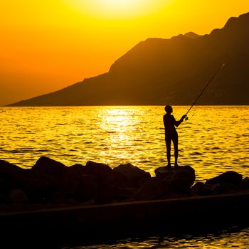 Fisherman silhouette on the beach at colorful sunset