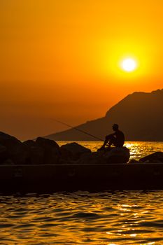 Fisherman silhouette on the beach at colorful sunset