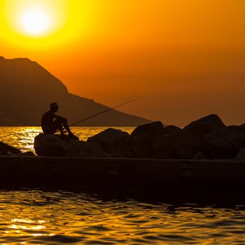 Fisherman silhouette on the beach at colorful sunset