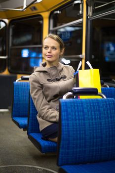 Pretty, young woman on a streetcar/tramway, during her evening commute home from work (color toned image; shallow DOF)