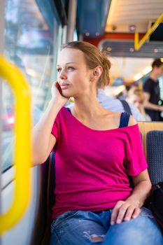 Pretty, young woman on a streetcar/tramway, during her commute from work/school (color toned image; shallow DOF)