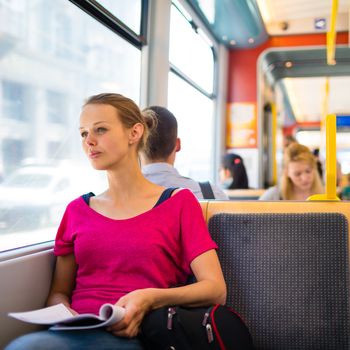 Pretty, young woman on a streetcar/tramway, during her commute to work/school (color toned image; shallow DOF)