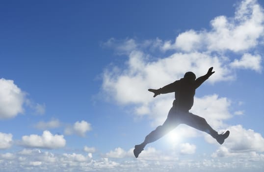 Silhouette of man jumping set against blue sky and clouds.