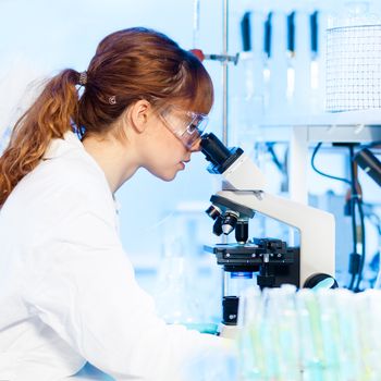 Attractive young female research scientist looking at the microscope slide in the life science (forensics, microbiology, biochemistry, genetics, oncology...)laboratory.
