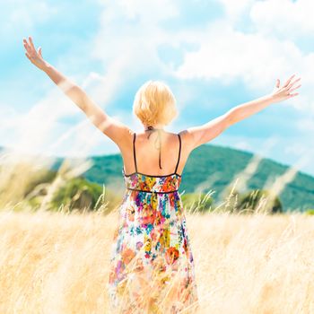 Lady enjoying the nature. Young woman arms raised enjoying the fresh air in summer meadow.