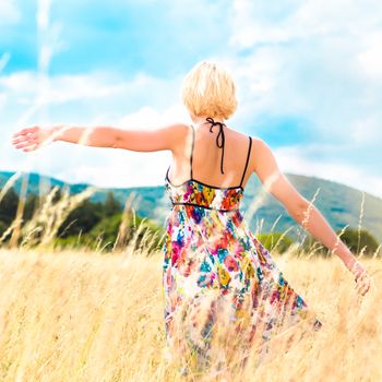 Lady enjoying the nature. Young woman arms raised enjoying the fresh air in summer meadow.