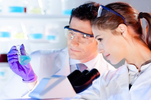 Chemical laboratory scene: attractive young student and her post doctoral supervisor scientist observing the green indikator solution color shift in glass flask.