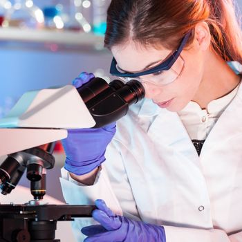 Attractive young scientist looking at the microscope slide in the forensic laboratory.