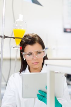 Attractive young female scientist checking experiment protocol at tablet laptop computer in the life science research laboratory (bichemistry, genetics, forensics, microbiology..)