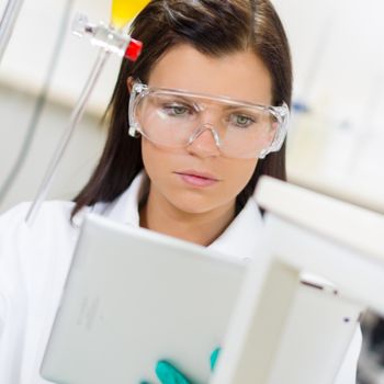 Attractive young female scientist checking experiment protocol at tablet laptop computer in the life science research laboratory (bichemistry, genetics, forensics, microbiology..)