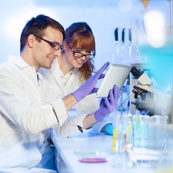 Attractive young female research scientist and her post doctoral male supervisor looking at the tablet in the life science (forensics, microbiology, biochemistry, genetics, oncology...)laboratory.