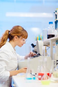 Focused attractive young life science professional measuring the absorbance of the solution in cuvette in the spectrophotometer. Focus on the researcher's face.