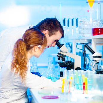 Attractive young female research scientist and her post doctoral male supervisor looking at the microscope slide in the life science (forensics, microbiology, biochemistry, genetics, oncology...)laboratory.