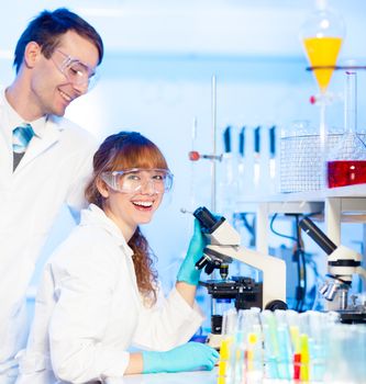 Attractive young female research scientist and her post doctoral male supervisor having fun looking at the microscope slide in the life science laboratory.