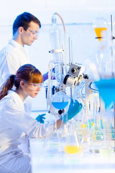 Chemical laboratory scene: attractive young PhD student and her post doctoral supervisor scientist observing the blue indicator color shift after the solution  destillation.