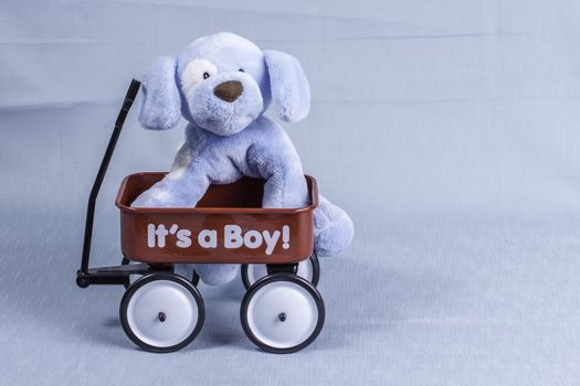 A stuffed animal dog sitting in a red wagon announcing the arrival of a newborn boy.