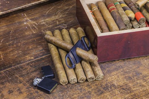 A group of cigars layed out on an old desk waiting to be cut and smoked.