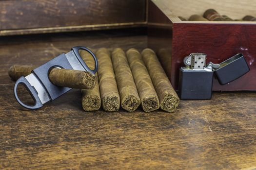 A group of cigars layed out on an old desk waiting to be cut and smoked.