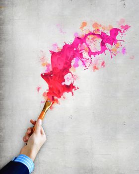 Close-up of human hand holding paint brush making colorful paint splashes