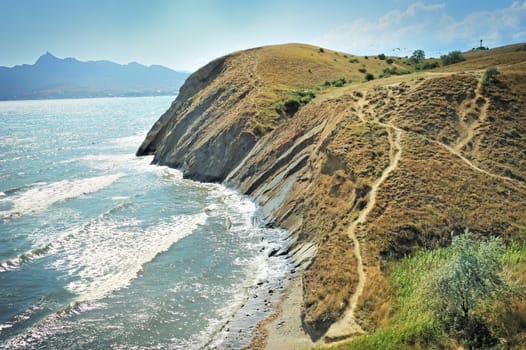 Steep cliff at the edge of the sea, against the backdrop of the Crimean Mountains.