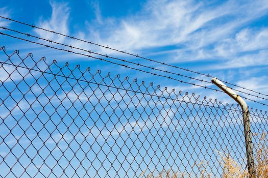Mesh fence with barbed wire on a background of blue sky