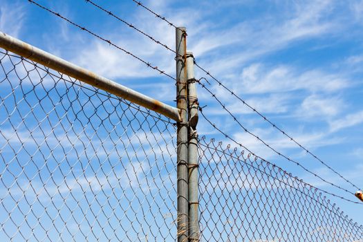 Mesh fence with barbed wire on a background of blue sky