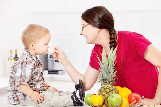 Mother feeding child with an apple in the kitchen