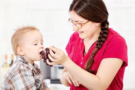 Mother feeding child with grapes in kitchen