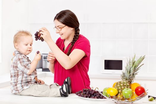 Mother feeding child with grapes in kitchen