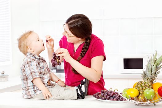 Mother feeding child with grapes in kitchen