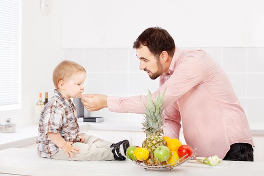 Father feeding child with apple in kitchen