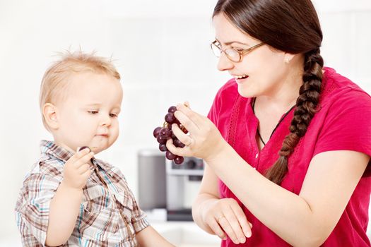 Mother feeding son with grapes in kitchen