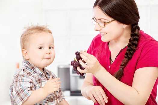 Mother feeding child with grapes in kitchen
