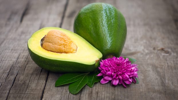 Avacado fruit with green leaves and flower on wood background