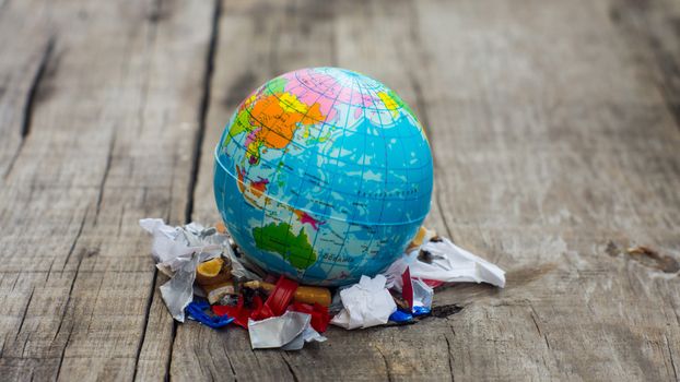 A globe standing of a pile of garbage on wood background. 