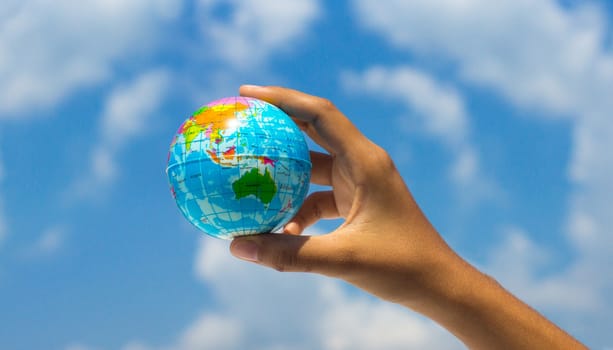 A person holding a globe with clouds in the background