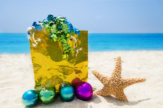 Starfish with Christmas balls and yellow gift bag on sandy beach in sunny day- holiday concept