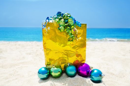 Yellow gift bag with Christmas balls on sandy beach in sunny day- holiday concept