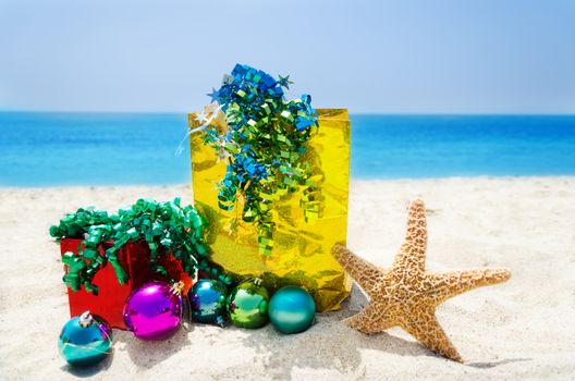 Starfish with Christmas balls, gift box and gift bag on sandy beach in sunny day- holiday concept