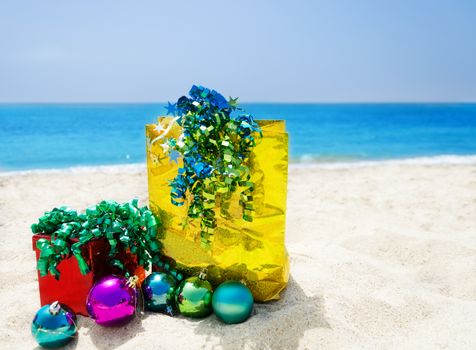 Red Gift box and gold gift bag with christmas balls on sandy beach in sunny day- holiday concept