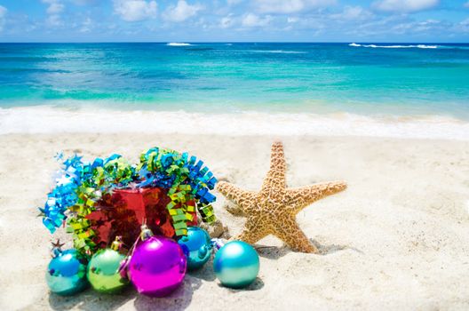 Starfish with Christmas balls and red gift box on sandy beach in sunny day- holiday concept