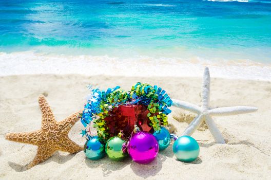Two Starfishes with Christmas balls and gift box on sandy beach in sunny day- holiday concept