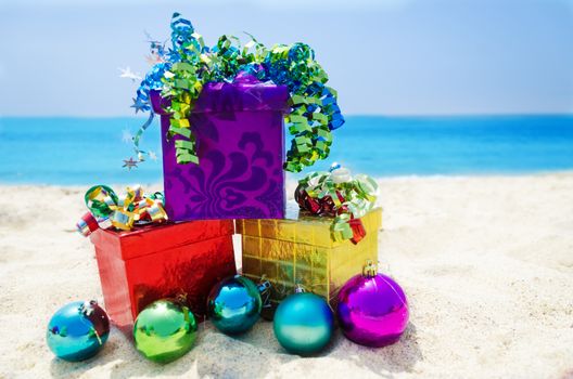 Three Gift boxes with Christmas balls on sandy beach in sunny day- holiday concept