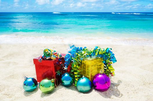 Two gift boxes with Christmas balls on sandy beach in sunny day- holiday concept