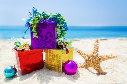 Starfish with Christmas balls and three gift boxes on sandy beach in sunny day- holiday concept