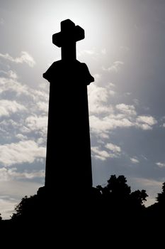 Tombstone cross in silhouette against dramatic sky at cemetery