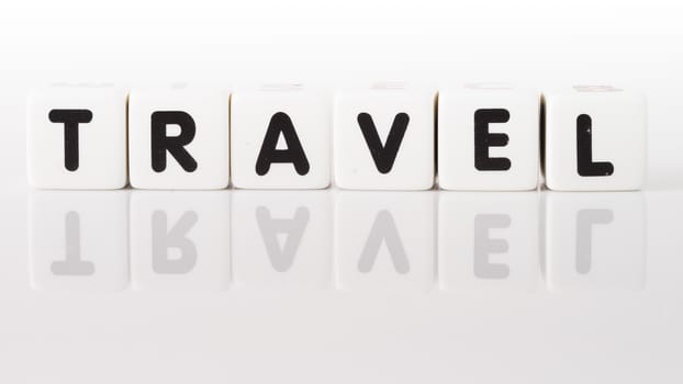 Travel spelled in dice letters reflected on white background.